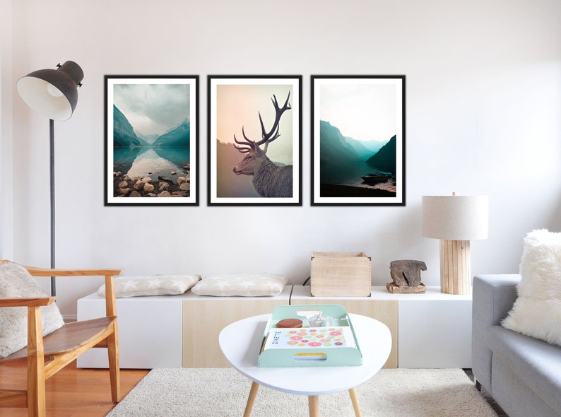 May include: Three framed landscape photographs of a mountain lake with a deer in the middle frame. The lake is a deep blue and the mountains are a soft green. The deer is looking to the right and has large antlers.