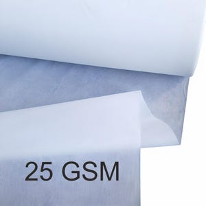 May include: A close-up of a roll of white fabric with a blue-grey layer visible underneath. The text "25 GSM" is printed in black at the bottom of the image. The fabric appears to be thin and lightweight.