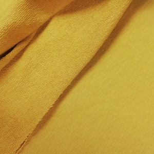 K&ouml;nnte beinhalten: Nahaufnahme eines gelben Stoffes mit strukturierter Oberfl&auml;che. Der Stoff ist in der Mitte gefaltet und bildet eine diagonale Linie.