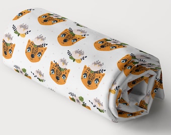 May include: White fabric with a repeating pattern of orange and black leopard faces with floral accents. The fabric is rolled up.
