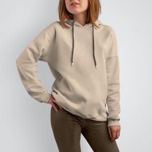 K&ouml;nnte beinhalten: Ein hellbeiger Hoodie mit einer Kapuze mit Kordelzug. Der Hoodie hat lange &Auml;rmel und eine lockere Passform.