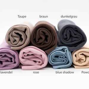 Könnte beinhalten: Acht Rollen Stoff in verschiedenen Farben, darunter Taupe, Braun, Dunkelgrau, Lavendel, Rose, Blauer Schatten und Puder. Der Stoff ist aufgerollt und übereinander gestapelt.