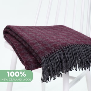 May include: A burgundy throw blanket made of 100% New Zealand wool with a dark gray fringe.