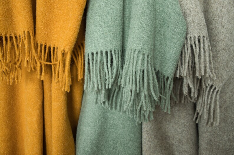 May include: Three woven blankets with fringe, one mustard yellow, one sage green, and one light gray.