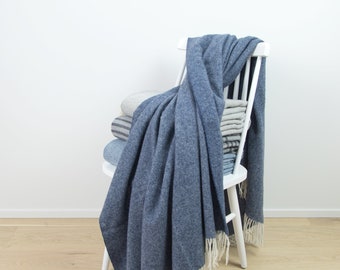 Puede incluir: Una manta de lana azul con flecos blancos drapeada sobre una silla de madera blanca. La manta está doblada y apilada en el asiento de la silla.