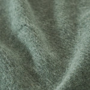 May include: Close-up of a soft, green fabric with a fuzzy texture. The fabric is wrinkled and has a subtle sheen.