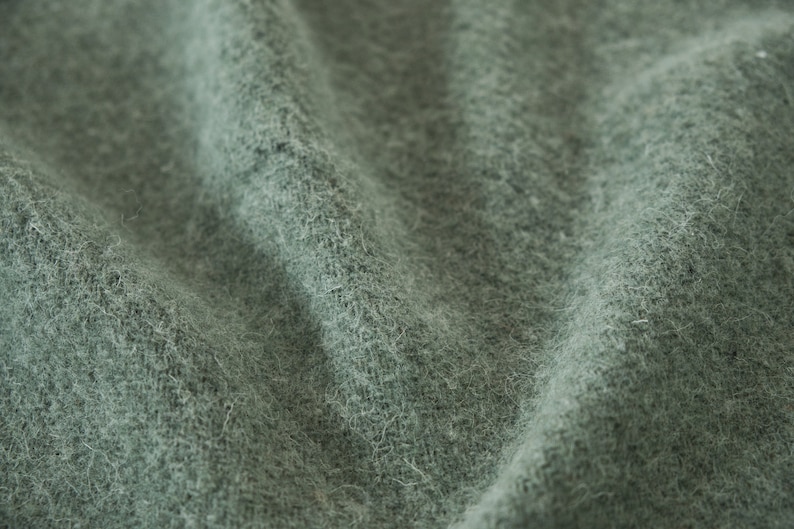 May include: Close-up of a soft, green fabric with a fuzzy texture. The fabric is wrinkled and has a subtle sheen.