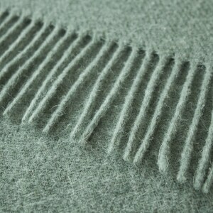 May include: Close-up of a soft, green knitted scarf with a fringe edge.