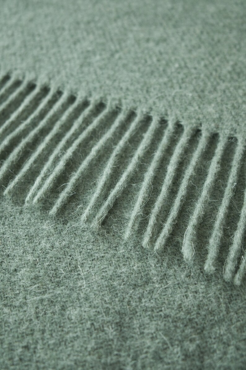 May include: Close-up of a soft, green knitted scarf with a fringe edge.
