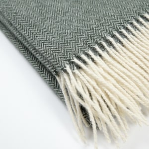 Puede incluir: Una suave manta de color verde con un patrón de espiga y flecos blancos.