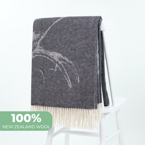 Può includere: Una coperta in lana grigio antracite con un design astratto bianco e un bordo a frangia. La coperta è realizzata in 100% lana della Nuova Zelanda.