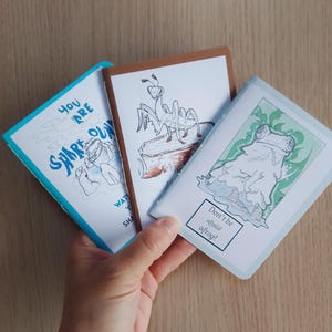 May include: Three illustrated cards with animal drawings and text. The first card has a blue border and says "You are shark-some". The second card has a brown border with an ant illustration. The third card has a light green border with a frog illustration and the text "Don't be afraid afrog!"