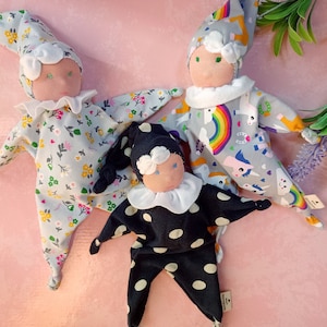 Può includere: Tre bambole di stoffa fatte a mano con diversi motivi. Una bambola indossa una stampa floreale grigia e bianca, un'altra indossa una stampa grigia e bianca con un arcobaleno e un design di unicorno, e la terza bambola indossa una stampa a pois neri e bianchi.