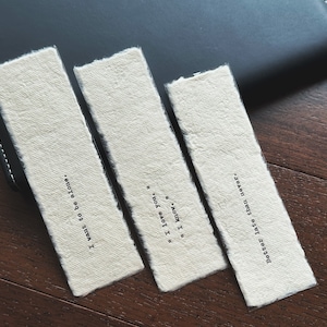 Könnte beinhalten: Drei weiße Papier-Lesezeichen mit schwarzem Text. Die Lesezeichen haben folgenden Text: "Ich möchte allein sein." "Ich liebe dich." "Besser spät als nie."
