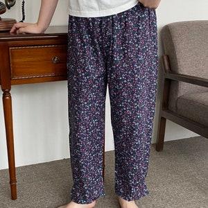 May include: Navy blue pajama pants with a delicate floral pattern in pink, white, and green. The pants have a comfortable, loose fit and a ruffled hem. The person is wearing a white t-shirt.