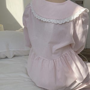 May include: A pink and white striped pajama top with a white lace collar. The top has a ruffled hem and long sleeves.