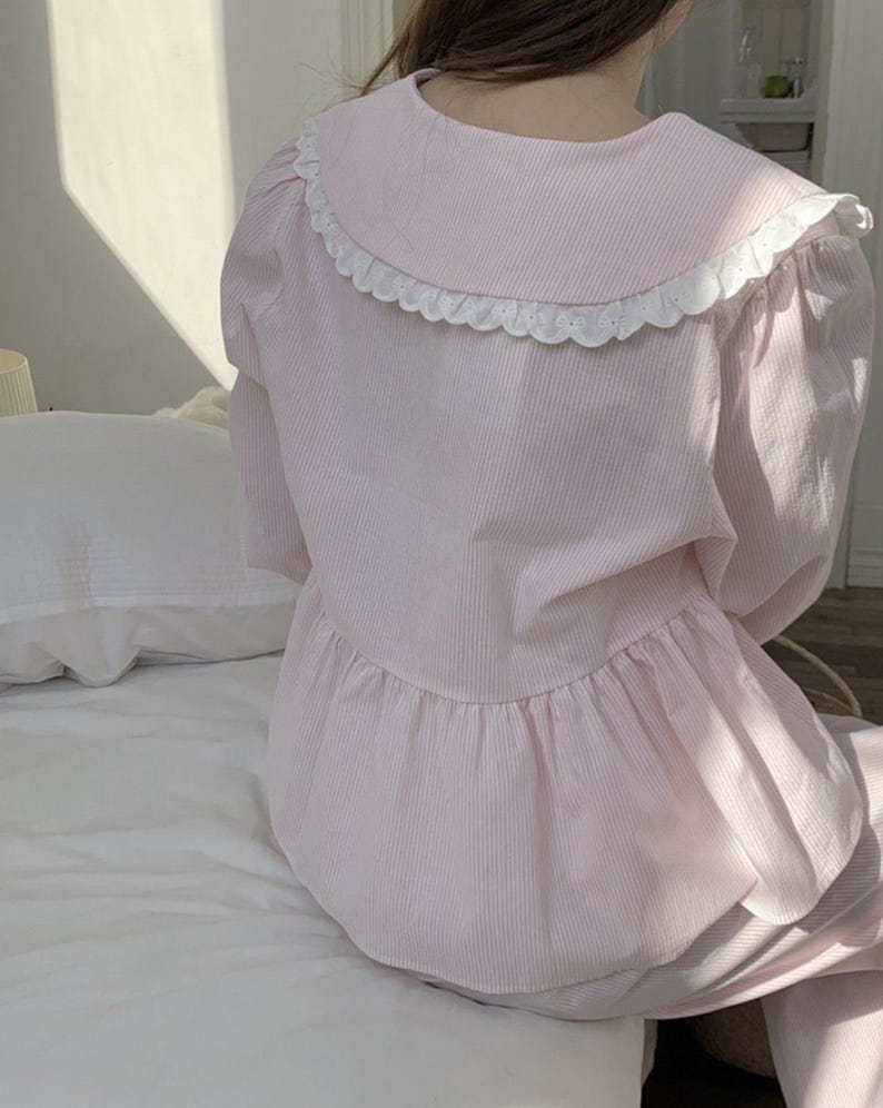 May include: A pink and white striped pajama top with a white lace collar. The top has a ruffled hem and long sleeves.