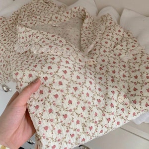 May include: A white button-up shirt with a delicate floral pattern in shades of pink and green. The shirt has a ruffled collar and a lace trim.