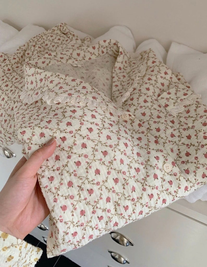 May include: A white button-up shirt with a delicate floral pattern in shades of pink and green. The shirt has a ruffled collar and a lace trim.