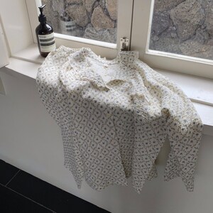 May include: A white button-down shirt with a floral pattern. The shirt has a ruffled collar and long sleeves.