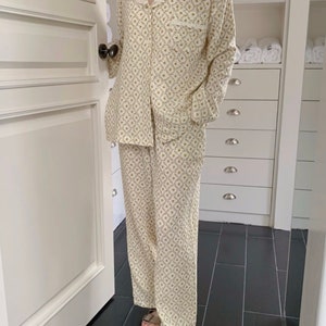 May include: A white pajama set with a floral pattern. The top has a lace trim collar and long sleeves. The pants are long and have a straight leg.