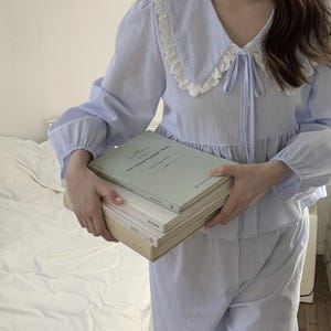 May include: A blue and white striped pajama set with a white lace collar and a bow tie. The top has long sleeves and the pants have a relaxed fit.