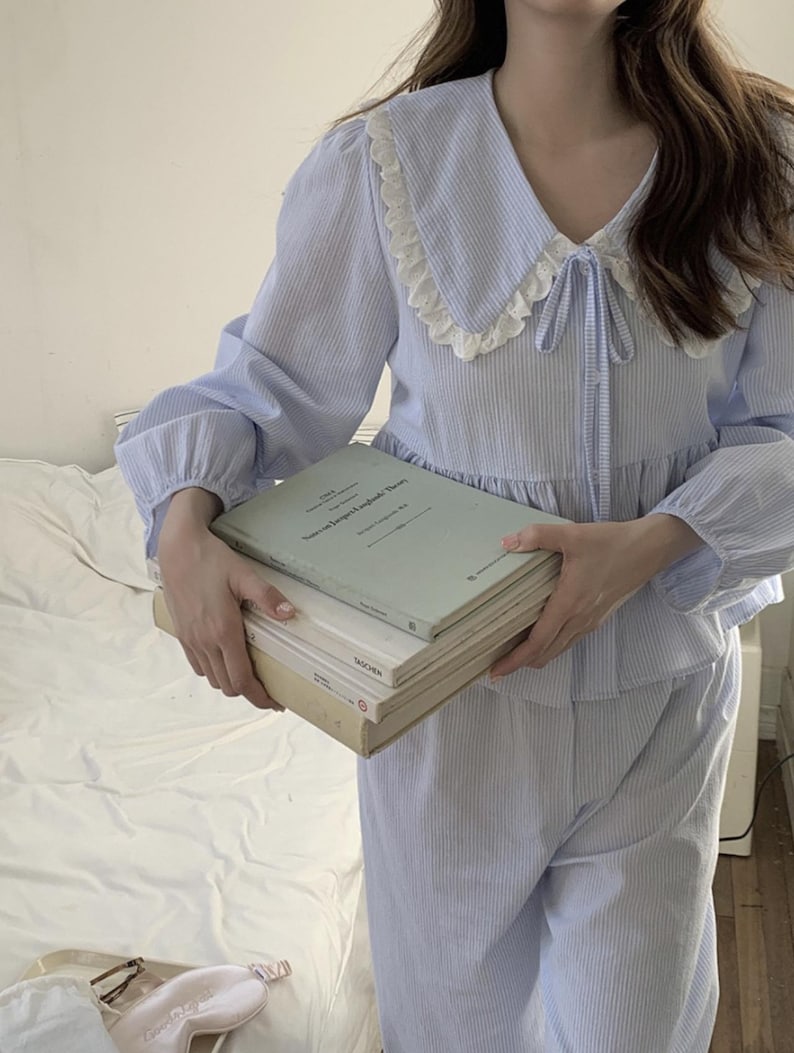 May include: A blue and white striped pajama set with a white lace collar and a bow tie. The top has long sleeves and the pants have a relaxed fit.