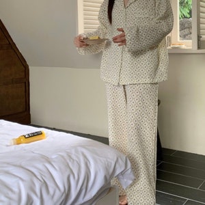 May include: A white pajama set with a floral pattern. The top has a collar and long sleeves. The pants are long and have a straight leg.