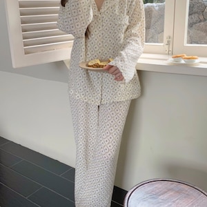 May include: A white pajama set with a floral pattern. The top has a collar and long sleeves. The pants are long and have a straight leg.
