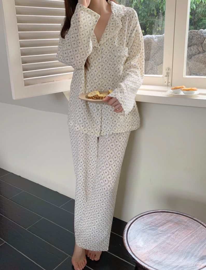 May include: A white pajama set with a floral pattern. The top has a collar and long sleeves. The pants are long and have a straight leg.