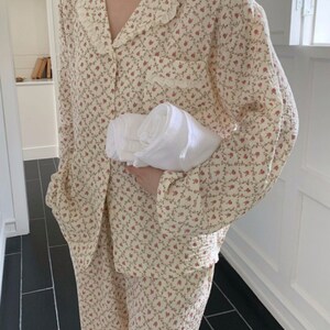 May include: A cream-colored pajama set with a floral print and a lace trim on the collar. The set includes a long-sleeved shirt and pants.