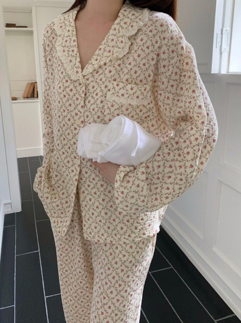 May include: A cream-colored pajama set with a floral print and a lace trim on the collar. The set includes a long-sleeved shirt and pants.