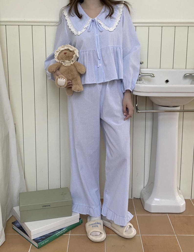 May include: A light blue pajama set with a white lace collar and a ruffled hem. The top has a button-up front and a bow tie. The pants are wide-legged and have a striped pattern.