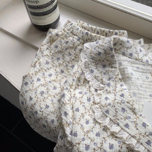 May include: A white cotton pajama top and shorts set with a floral print and lace trim. The top has a collar and the shorts have an elastic waistband.