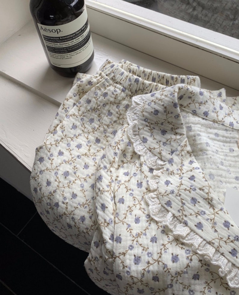 May include: A white cotton pajama top and shorts set with a floral print and lace trim. The top has a collar and the shorts have an elastic waistband.