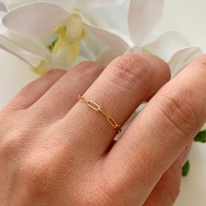 May include: A delicate gold chain ring with a simple design. The ring is worn on a finger and is a minimalist piece of jewelry.