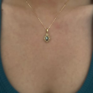 May include: A gold chain necklace with a pendant featuring a grey oval gemstone surrounded by a gold beaded border.