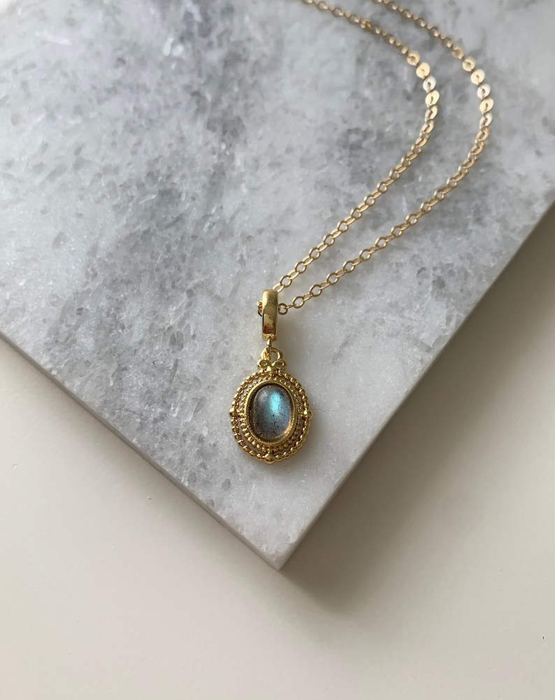 May include: A gold chain necklace with a pendant featuring a blue-grey oval gemstone set in a gold filigree frame.
