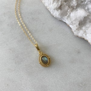 May include: A gold chain necklace with a pendant featuring a green and blue oval gemstone set in a gold filigree frame.
