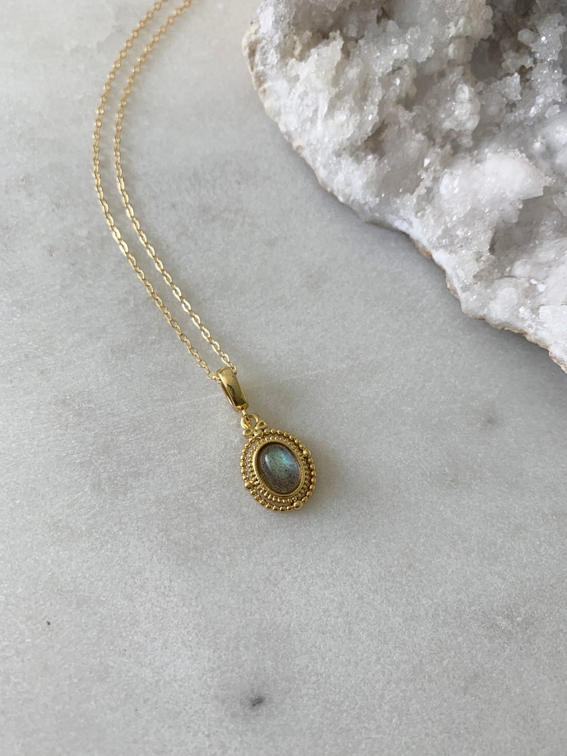 May include: A gold chain necklace with a pendant featuring a green and blue oval gemstone set in a gold filigree frame.