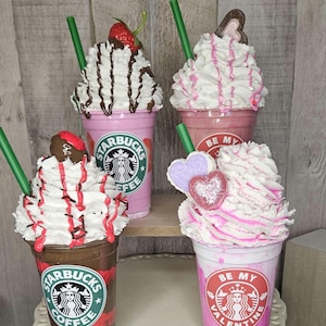 Puede incluir: Cuatro Frappuccinos Starbucks rosas y marrones decorados para el D&iacute;a de San Valent&iacute;n. Las bebidas tienen crema batida, salsa de chocolate y caramelos en forma de coraz&oacute;n. Las tazas tienen el logotipo de Starbucks y el texto "Starbucks Coffee" y "Be My Valentine".