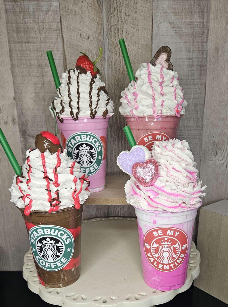 Puede incluir: Cuatro Frappuccinos Starbucks rosas y marrones decorados para el D&iacute;a de San Valent&iacute;n. Las bebidas tienen crema batida, salsa de chocolate y caramelos en forma de coraz&oacute;n. Las tazas tienen el logotipo de Starbucks y el texto "Starbucks Coffee" y "Be My Valentine".