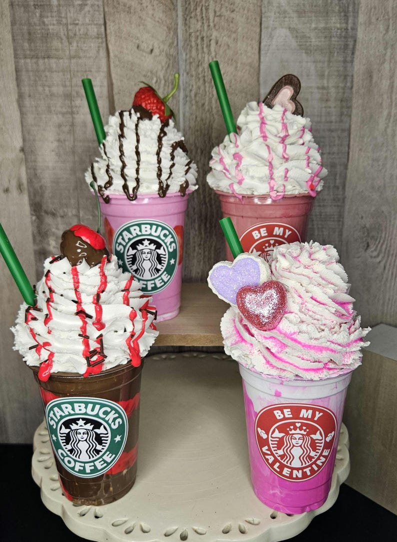 Puede incluir: Cuatro bebidas de caf&eacute; decoradas con crema batida y coberturas. Las bebidas est&aacute;n en vasos de pl&aacute;stico transparente con una base rosa, marr&oacute;n y blanca. Los vasos tienen el logotipo de Starbucks y el texto "Be My Valentine" y "Starbucks Coffee".