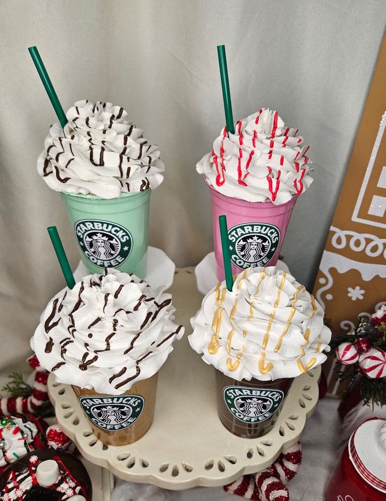Puede incluir: Cuatro Frappuccinos Starbucks con crema batida y diferentes ingredientes. Los Frappuccinos est&aacute;n en vasos de pl&aacute;stico transparente con tapas verdes y el logotipo de Starbucks. Los ingredientes incluyen llovizna de chocolate, chispas rojas, llovizna de caramelo y virutas de chocolate.
