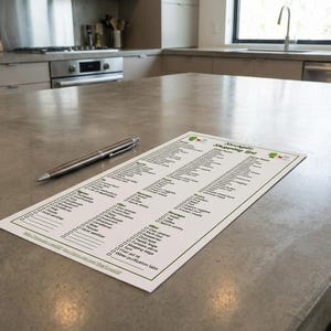 K&ouml;nnte beinhalten: Eine gedruckte Einkaufsliste mit dem Titel "Stockpile Shopping List" mit einem Stift auf einer grauen Arbeitsplatte. Die Liste ist mit verschiedenen Lebensmitteln gef&uuml;llt. Der Stift ist silber und schwarz. Die K&uuml;che hat Edelstahlger&auml;te.
