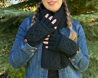May include: A black knitted scarf and matching fingerless gloves featuring a textured cable knit pattern. The gloves are accented with small, round wooden buttons at the wrists, providing a coordinated look for cold weather accessories.