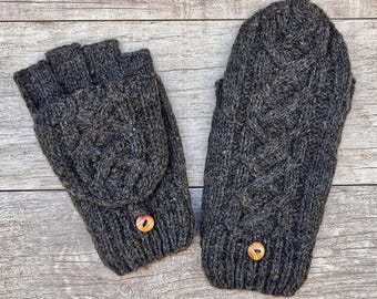 May include: A pair of dark charcoal gray knit fingerless gloves that convert into mittens. Each glove features a textured cable knit pattern and a single round wooden button attached to the ribbed cuff area for securing the flap.