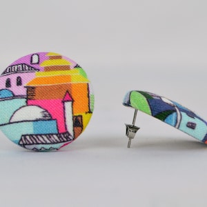Puede incluir: Un par de pendientes de botón de tela coloridos con un diseño geométrico de edificios y una cúpula. Los pendientes son una mezcla vibrante de rosa, amarillo, azul, verde y naranja.