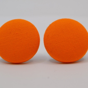 Op de afbeelding: Twee ronde, met stof beklede knopen in een levendige, effen oranje kleur. Elke knoop heeft een gladde, bolvormige vorm met een zichtbare geweven textielstructuur over het oppervlak, naast elkaar gepresenteerd tegen een neutrale achtergrond.