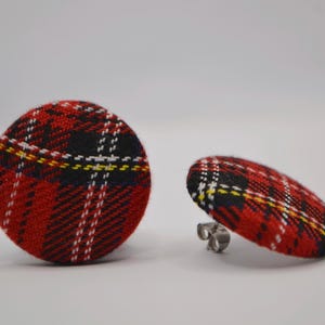 Op de afbeelding: Een paar ronde oorstekers met een rood, zwart, wit en geel geruit patroon. Eén oorbel staat rechtop, de andere is gekanteld en toont de zilveren pin. De oorbellen staan tegen een effen witte achtergrond.